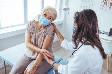 Klinikteki yaşlı hastasının elini tutan genç bayan doktor.