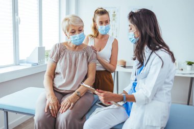 Kadın doktordan kıdemli kadın ve yetişkin kızı. Profesyonel gülümseyen doktor, kıdemli bir hasta ve kızıyla hastanede buluşuyor.