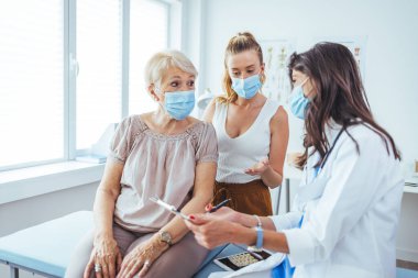 Kızın check-up randevusunda annesiyle oturuyor. Profesyonel gülümseyen doktor, kıdemli bir hasta ve kızıyla hastanede buluşuyor.