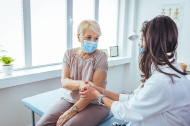Klinikteki yaşlı hastasının elini tutan genç bayan doktor.