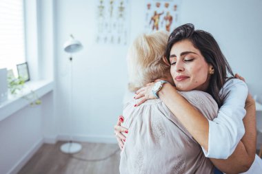 Klinikte kıdemli hastasına sarılan neşeli bir kadın doktorun portresi.