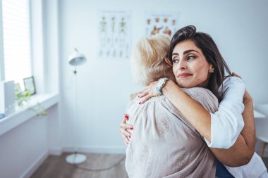 Klinikte kıdemli hastasına sarılan neşeli bir kadın doktorun portresi.