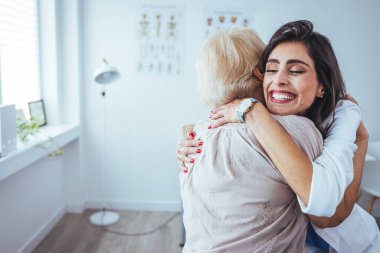 Klinikte kıdemli hastasına sarılan neşeli bir kadın doktorun portresi.