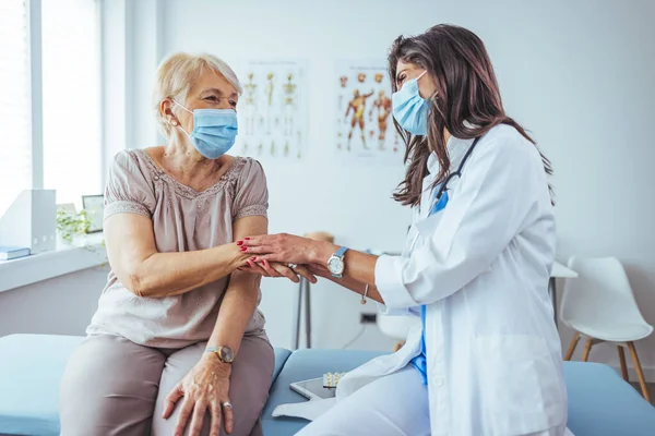 Klinikteki yaşlı hastasının elini tutan genç bayan doktor.