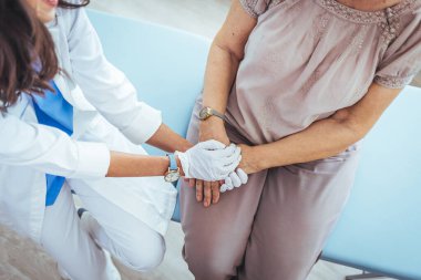 Klinikteki yaşlı hastasının elini tutan genç bayan doktor.