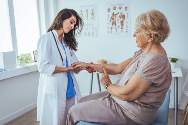 Klinikteki yaşlı hastasının elini tutan genç bayan doktor.