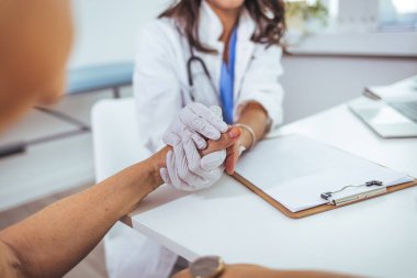 Tanımlanamayan bir kadın hemşirenin hastanede bir hastayı rahatlatırken görüntüsü. Doktor kadın hastasına güvence verdiği için el ele tutuşuyor. İhtiyaç olduğunda bakım ve rahatlık sunuyor.