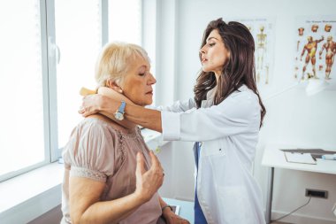 Boynundan yaralanan yaşlı bir kadına yardım eden ve yakasına sağlık sigortası ve ilaç konsepti koyan bir kadın doktorun portresi. Doktor kıdemli bir hastaya boyunluk takıyor. 