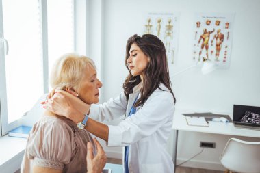 Doktor, yaşlı bir kadının röntgenini inceliyor. Rahim boynu tasması takıyor ve ciddi bir boyun yaralanması geçiriyor. Yetişkin bir kadının kadın doktor muayenehanesini ziyaret ederken fotoğrafı.
