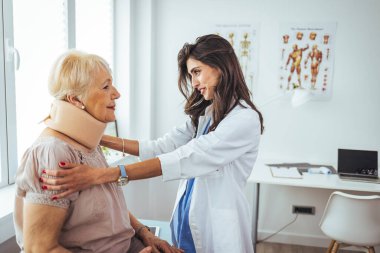 Doktor, yaşlı bir kadının röntgenini inceliyor. Rahim boynu tasması takıyor ve ciddi bir boyun yaralanması geçiriyor. Yetişkin bir kadının kadın doktor muayenehanesini ziyaret ederken fotoğrafı.