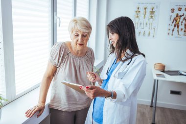 Kıdemli bir kadın, doktorunun muayenesi sırasında doktoruyla konuşur. Kıdemli hasta orta yaşlı kadın doktoru dikkatle dinler. Doktor panoda bir şeyi açıklıyor.