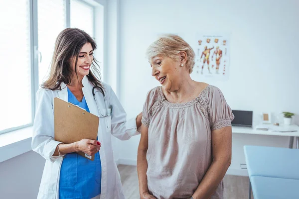 Happy senior woman visiting doctor and listening to her advice during appointment. Nurse Showing Patient Test Results On Clipboard. Doctor and patient standing in doctor\'s office