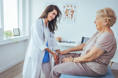 Fiziksel doktor hasta dizindeki sorunlara danışmanlık yapıyor. Fizik tedavi konsepti. Doktor nazikçe dizin ve diz kapağının etrafındaki tendonlara dokunuyor ve ağrının sebebini belirlemeye çalışıyor..