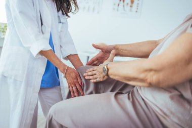Son sınıf öğrencisinin diz ağrısı çektiği bir fotoğraf. Doktorun muayenehanesinde erkek bir doktor tarafından muayene ediliyor. Doktor hassas bölgeye dokunuyor ve acının nedenini belirlemeye çalışıyor..