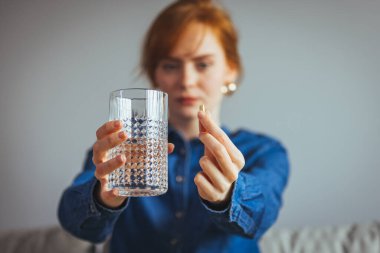 Kadın yüzü ve hapın yakın plan görüntüsü. Hasta genç bir kadın, elinde beyaz yuvarlak haplar tutuyor ve iyileşme için doktor reçetesi olarak ilaç alıyor.. 