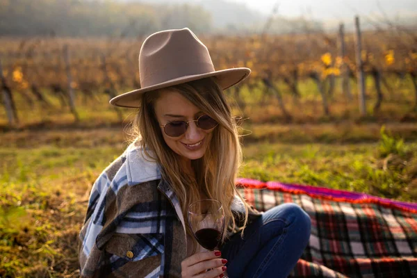 Woman with hat holding wine glass and looking at camera. Winegrowers at wineyard tasting red wine. Close up face of smiling woman raising a glass of red wine. Woman drinking red wine