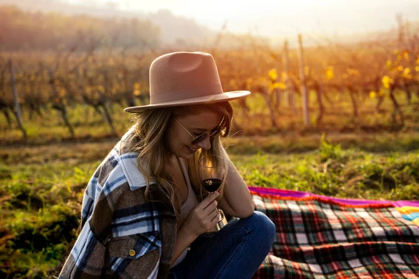 Woman tasting wine in vineyard. She is showing glass of wine to camera. Beautiful young woman with glass of wine in vineyard on sunny day. Portrait of a gorgeous brunette woman having wine fun in the vineyards.