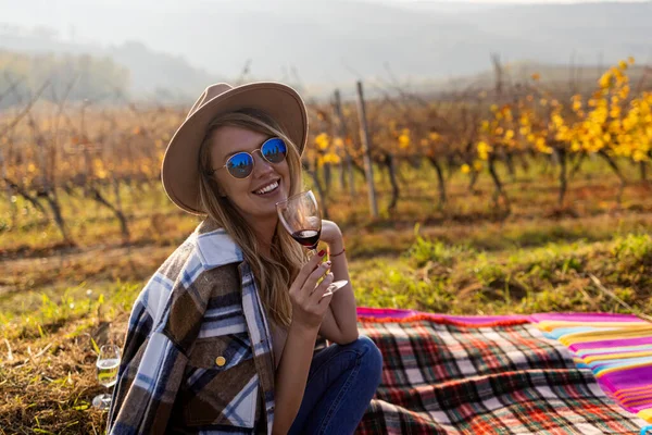 ブドウ畑でワインを味わう女性 彼女はワインのグラスをカメラに見せている 晴れた日にブドウ畑でワインのガラスを持つ美しい若い女性 ブドウ畑でワインを楽しんでいる豪華なブルネットの女性の肖像画 — ストック写真