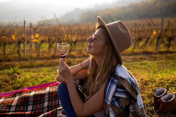 stock image Woman tasting wine in vineyard. She is showing glass of wine to camera. Beautiful young woman with glass of wine in vineyard on sunny day. Portrait of a gorgeous brunette woman having wine fun in the vineyards.