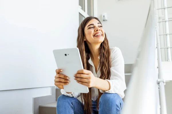 白いオフィスの背景に隔離されたタブレットコンピュータを使用して若い女性を笑顔 若い女子大生が階段にタブレットを使っています デジタルタブレットを使用して魅力的な若い女性 — ストック写真