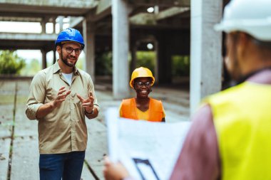 İnşaat halindeki yeni binanın planlarıyla mutlu bir mühendislik ekibi. Başarılı mühendisler inşaat alanında çalışıyor.