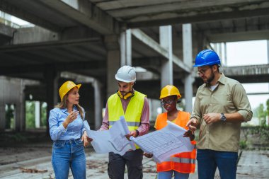 İnşaat halindeki yeni binanın planlarıyla mutlu bir mühendislik ekibi. Başarılı mühendisler inşaat alanında çalışıyor.