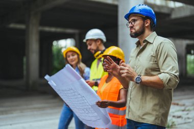 İnşaat halindeki yeni binanın planlarıyla mutlu bir mühendislik ekibi. Başarılı mühendisler inşaat alanında çalışıyor.