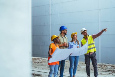 İnşaat halindeki yeni binanın planlarıyla mutlu bir mühendislik ekibi. Başarılı mühendisler inşaat alanında çalışıyor.