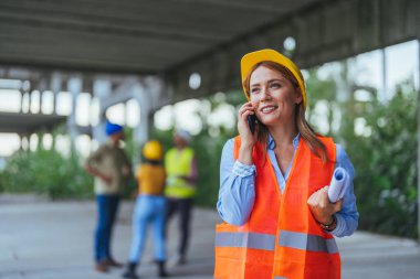 Beyaz kadın işçi inşaat alanında akıllı telefon kullanıyor.