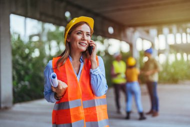 Beyaz kadın işçi inşaat alanında akıllı telefon kullanıyor.