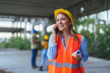 Beyaz kadın işçi inşaat alanında akıllı telefon kullanıyor.