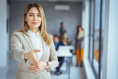 Bulanık ofiste arka planda iş arkadaşlarıyla el sıkışma işareti gösteren mutlu beyaz iş kadını.