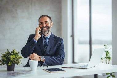 Ofiste çalışırken gülümseyen beyaz iş adamı akıllı telefondan konuşuyor.