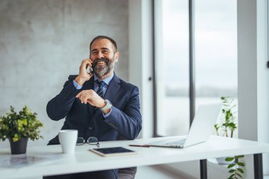 Ofiste çalışırken gülümseyen beyaz iş adamı akıllı telefondan konuşuyor.