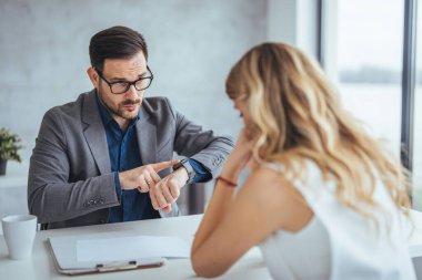 Kafkas işadamı ofis masasında çalışırken iş kadınına zaman gösteriyor.