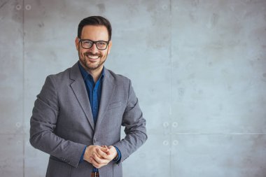 Başarılı, genç, sakallı, esmer, yetişkin, iş adamı, iş adamı, sıradan giysiler içinde modern merkez büroda kollarını kavuşturmuş duruyor ve kameraya bakıyor.