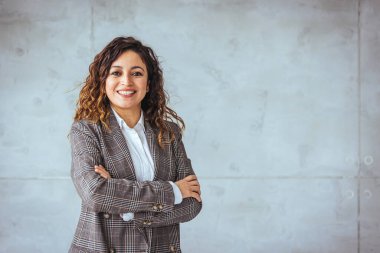 Kollarını kavuşturup kameraya bakan genç bir kadının portresi. Yaratıcı ofiste duran mutlu kız. Fotokopi alanı olan başarılı bir iş kadını.