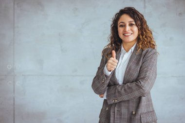 Modern ofiste kameraya bakan orta yaşlı bir iş kadınının portresi. Cam duvara yaslanırken kollarını kavuşturan kendine güvenen bir iş kadını. Fotokopi odasıyla resmi kıyafetler içinde gülümseyen gururlu esmer kadın..