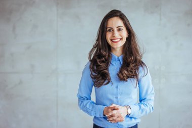 Modern bir ofiste duran kendine güvenen genç bir iş kadınının fotoğrafı. Modern ofiste kameraya bakan orta yaşlı bir iş kadınının portresi. Kollarını kavuşturmuş kendine güvenen bir iş kadını. 