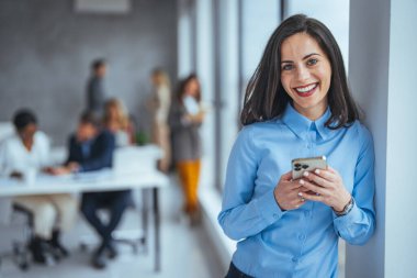 Sıradan giyimli genç bir kadın cep telefonunu kullanarak iş yerinde bir şeyler okuyor. Genç modern iş arkadaşları ofiste vakit geçirirken gündelik kıyafetlerini giyerler. Sadece bir mesaj önemli bir şey getirdi.