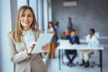 Dijital tablet kullanan genç bir iş kadınının fotoğrafı. Modern bir ofisteki masasında dijital tablet kullanan bir iş kadını fotoğrafı. Ofiste tablet kullanan gülümseyen genç bir iş kadınının portresi 