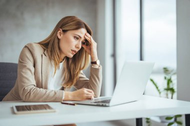 Ofiste çalışırken stresli görünen genç bir iş kadınının fotoğrafı. Dizüstü bilgisayardan çalışan stresli iş kadını endişeli, yorgun ve bunalmış görünüyor. 