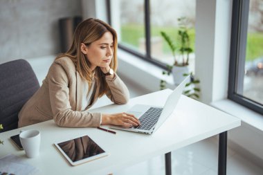 Ofiste çalışırken stresli görünen genç bir iş kadınının fotoğrafı. Dizüstü bilgisayardan çalışan stresli iş kadını endişeli, yorgun ve bunalmış görünüyor. 