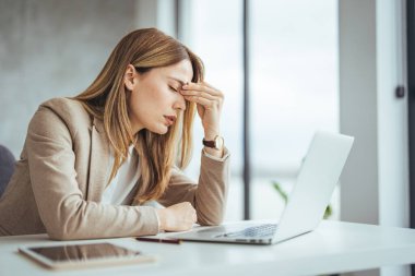 Yorgun işkadını modern ofiste having bir baş ağrısı. Ofis Masası duygu yorgun baş üzerine gözlük ile çalışan olgun yaratıcı kadın. Masaüstü bilgisayarda overworking süre rahat iş kadın duygu göz ağrısı vurguladı.