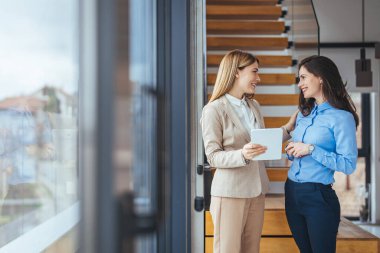 Dijital tablet üzerinde çalışan iki genç kadının fotoğrafı. Yaratıcı kadın yöneticiler ofiste buluşup tablet bilgisayar kullanıyor ve gülümsüyorlar. Dijital tablet tutan iki iş kadını