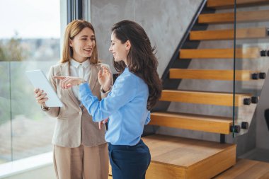 İş yerinde iş birliği yaparken iki iş kadınının dijital tablet kullanması. Tablet bilgisayara bakan bayan meslektaşlar. Dijital tablete bakıp yeni projeyi tartışan iki iş kadınının portresi.