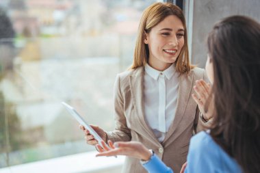 İş yerinde iş birliği yaparken iki iş kadınının dijital tablet kullanması. Tablet bilgisayara bakan bayan meslektaşlar. Dijital tablete bakıp yeni projeyi tartışan iki iş kadınının portresi.