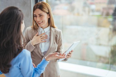 Dijital tablet bilgisayar kullanarak birlikte çalışan iki iş kadını bir iş projesi hakkında konuşuyor. Kadın yöneticilerden oluşan küçük yaratıcı çeşitlilik ekibi ofiste çalışıyor..