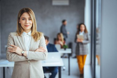 Kollarını kavuşturup kameraya bakan genç bir kadının portresi. Yaratıcı ofiste duran mutlu kız. Fotokopi odasında başarılı bir iş kadını duruyor. Şehirli mutlu iş kadını