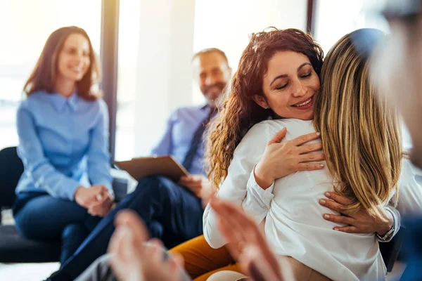 The two women are attending a group therapy session. They are showing support and kindness. Portrait of female psychologist embracing young woman during therapy session in support group